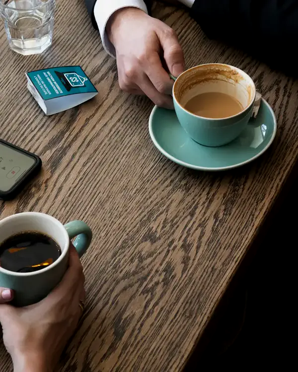 Zwei Menschen sitzen bei Kaffee an einem Tisch und sprechen miteinander.